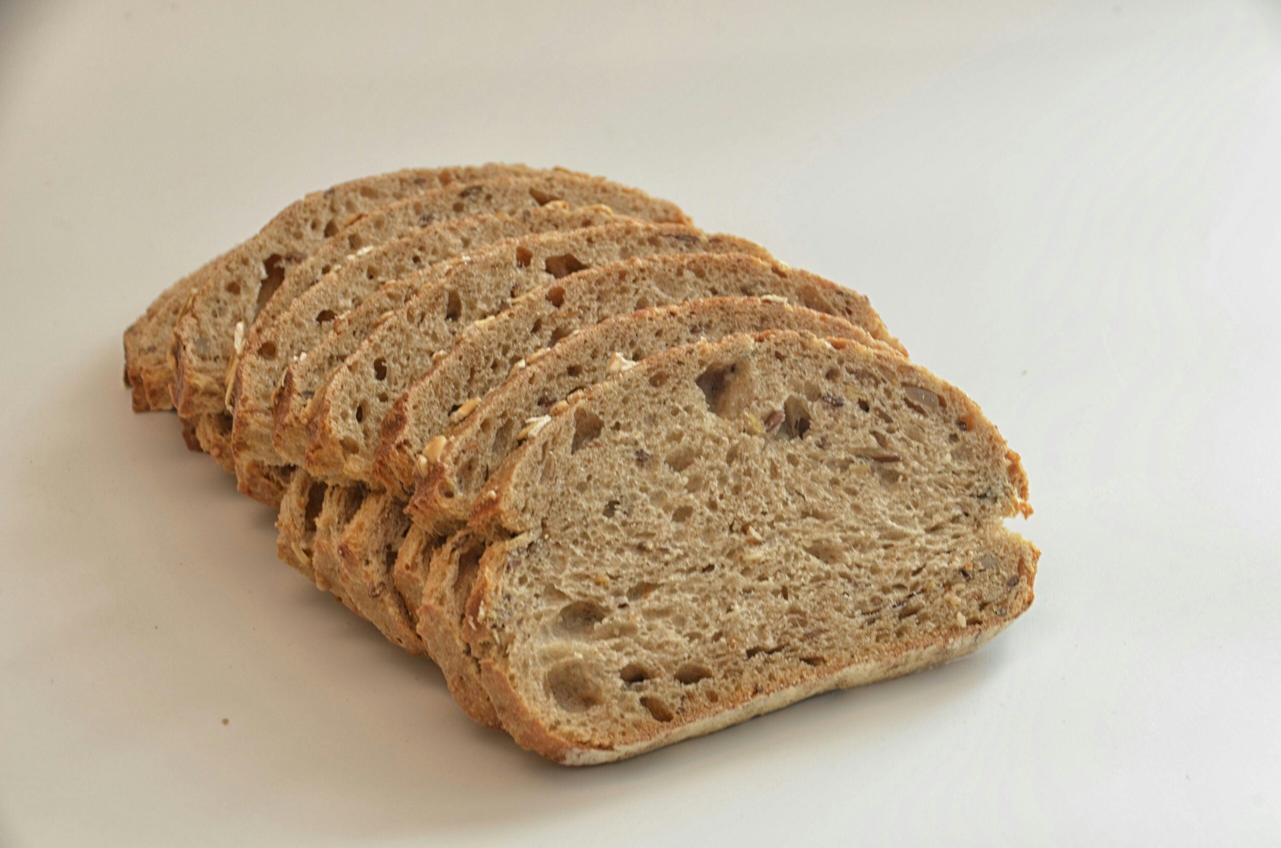 Close-up of sliced whole wheat bread on a white surface, showcasing texture and freshness.